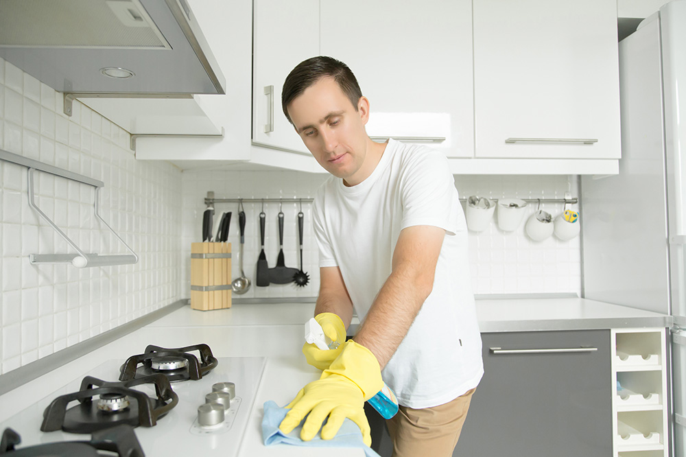 Young serious man wearing rubber yellow gloves cleaning the stov